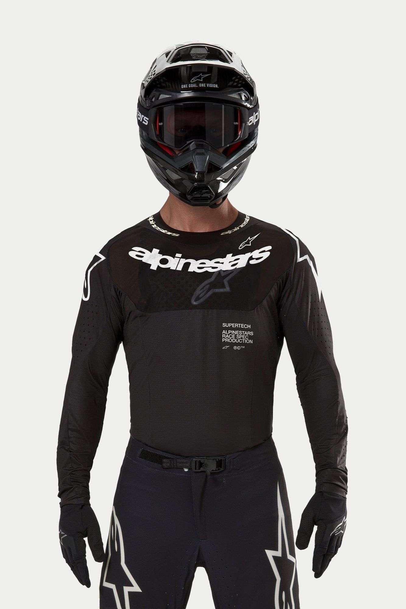 Pilote de motocross portant le maillot Alpinestars Supertech Ward 2024 noir, coupe de course athlétique avec logo Alpinestars blanc sur la poitrine, perforations découpées au laser et inscription 'Supertech Race Spec', associé à un casque et des lunettes noirs pour la course tout-terrain