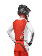 Motocross rider wearing the 2024 Supertech Ward Jersey in White Hot Orange, rear view showing orange back panel and white sleeves with black Alpinestars branding, paired with matching pants and a black helmet, coordinated professional gear for off-road racing