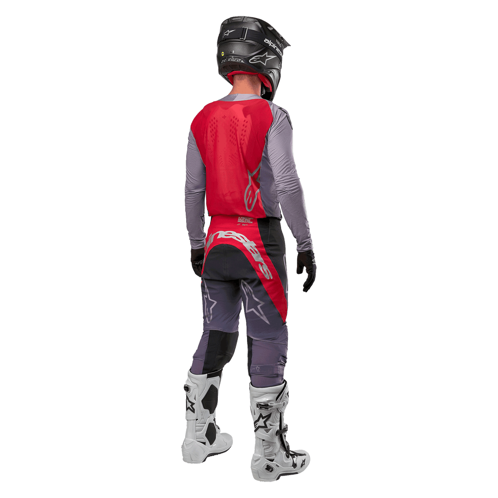 Maillot Alpinestars Supertech Dade 2024, maillot de motocross, rouge Iron Red Berry et gris, vue de dos sur un pilote, avec un panneau dorsal rouge, un logo gris et des manches grises, porté avec un pantalon de course coordonné gris et rouge, des bottes blanches et un casque noir, équipement tout-terrain professionnel.