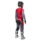 Maillot Alpinestars Supertech Dade 2024, maillot de motocross, rouge Iron Red Berry et gris, vue de dos sur un pilote, avec un panneau dorsal rouge, un logo gris et des manches grises, porté avec un pantalon de course coordonné gris et rouge, des bottes blanches et un casque noir, équipement tout-terrain professionnel.