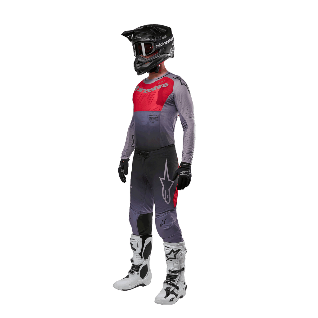 Pilote de motocross portant une tenue de course complète, maillot Alpinestars 2024 Supertech Dade en Iron Red Berry et gris, pantalon gris assorti avec des accents rouges, casque noir avec masque, bottes blanches et noires, gants noirs, tenue coordonnée pour la course tout-terrain