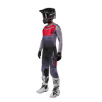 Pilote de motocross portant une tenue de course complète, maillot Alpinestars 2024 Supertech Dade en Iron Red Berry et gris, pantalon gris assorti avec des accents rouges, casque noir avec masque, bottes blanches et noires, gants noirs, tenue coordonnée pour la course tout-terrain