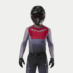 Pilote de motocross portant le maillot Alpinestars Supertech Dade 2024 en Iron Red Berry, doté d'un panneau rouge sur la poitrine et de manches grises avec logos argentés, porté avec un pantalon assorti, un casque noir et des gants noirs, équipement de course tout-terrain professionnel