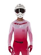 Pilote de motocross portant le maillot Alpinestars Supertech Dade 2024 en Red Berry Lilac, pantalon assorti, casque blanc avec lunettes noires et gants rouges, tenue de course professionnelle coordonnée avec des tons dégradés de rose et de rouge
