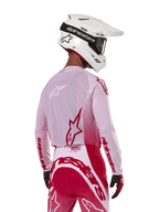Pilote de motocross vu de dos portant le maillot Alpinestars 2024 Supertech Dade en Red Berry Lilac, avec panneaux en maille respirante et logos Alpinestars rouges, assorti d'un pantalon rouge et lilas et d'un casque Alpinestars blanc avec lunettes, équipement de course tout-terrain professionnel