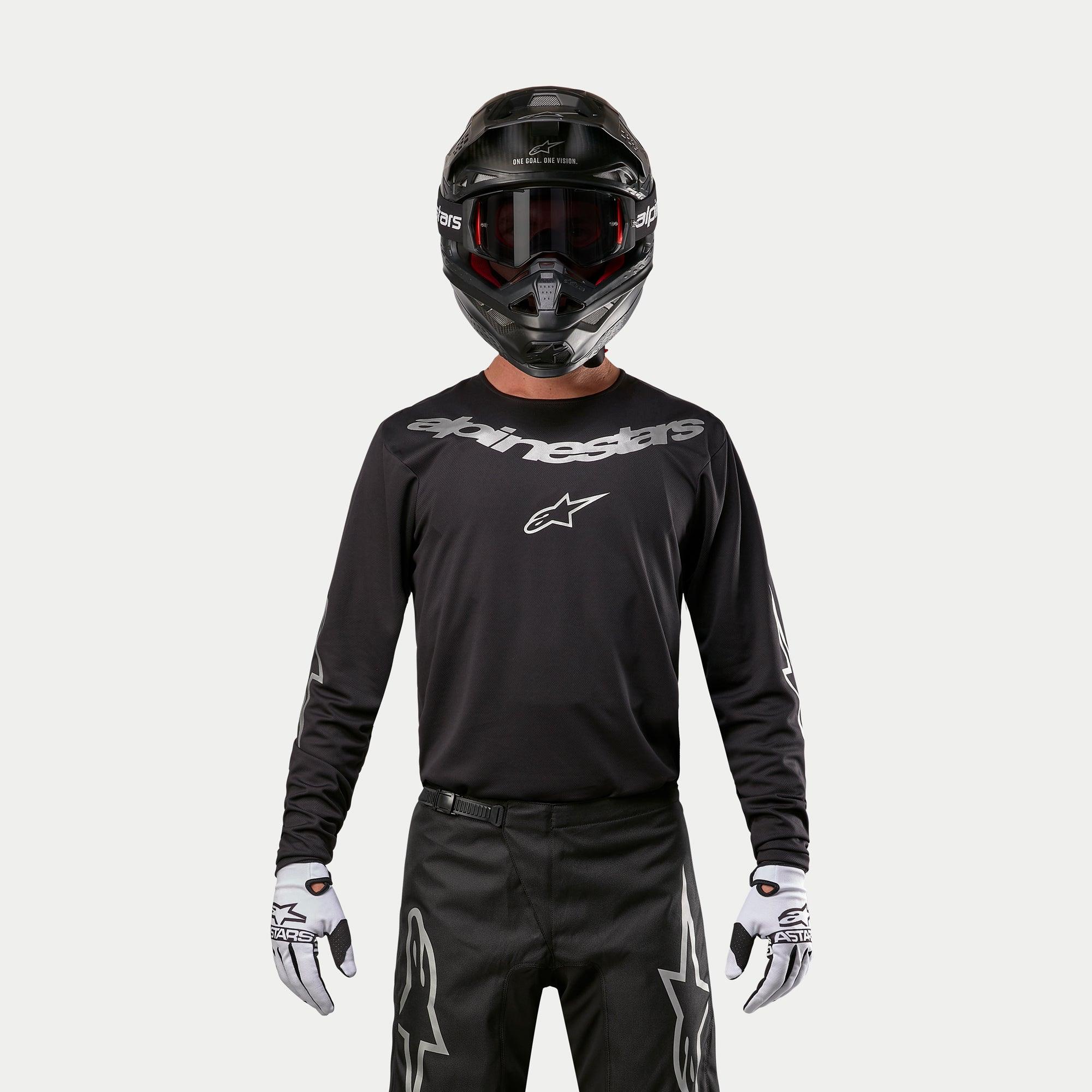 Maillot Alpinestars Fluid Graphite 2024, maillot de motocross noir et argent, porté par un pilote avec un casque noir et des lunettes rouges, logo Alpinestars argenté sur la poitrine, coordonné avec un pantalon noir et des gants blancs pour la performance tout-terrain
