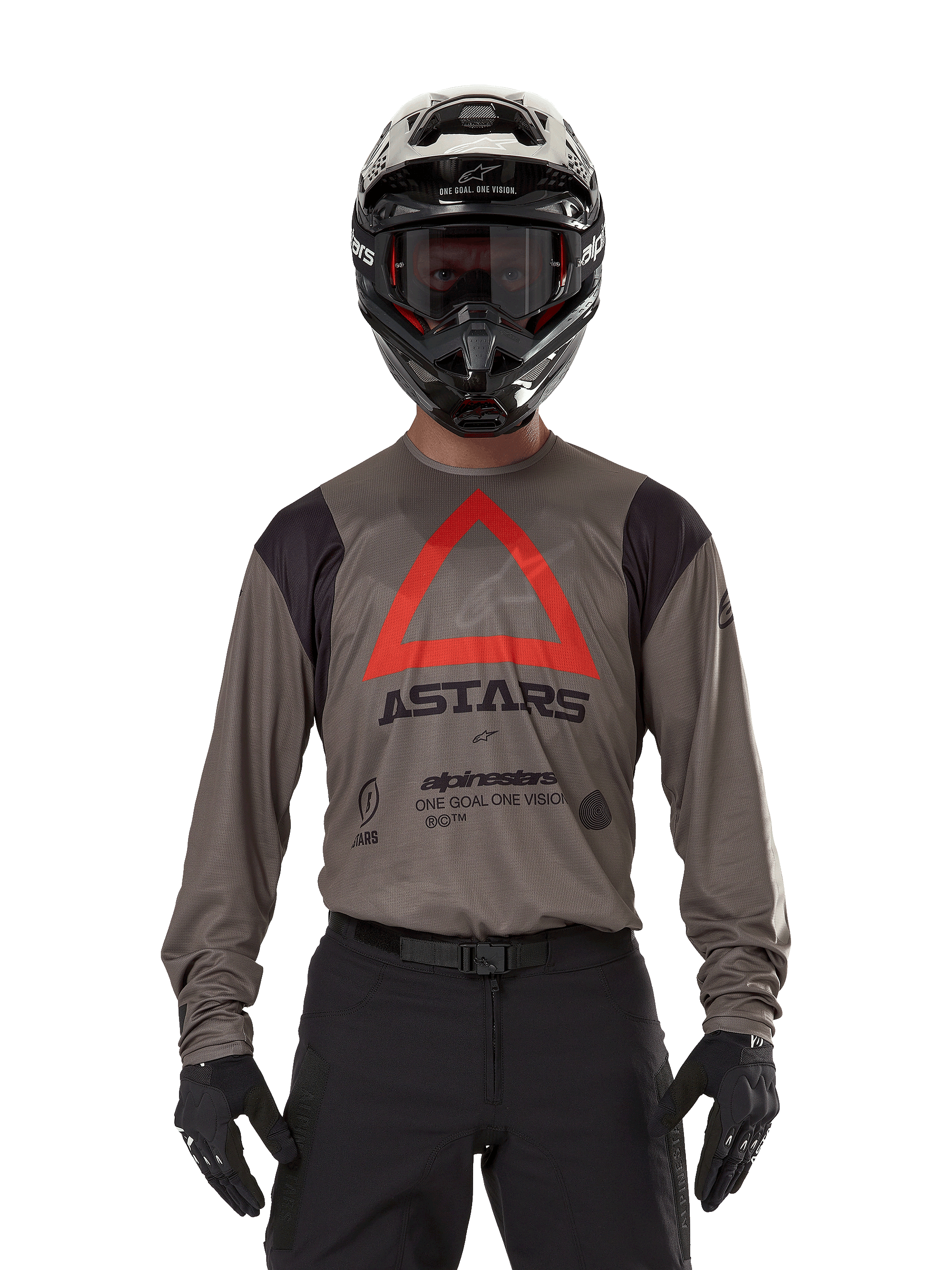 Motocross rider wearing Alpinestars Techdura Jersey in Falcon Brown, featuring a prominent red triangle and 'ASTARS' branding on the chest, paired with black pants, a black helmet with goggles, and black gloves, complete enduro racing outfit.
