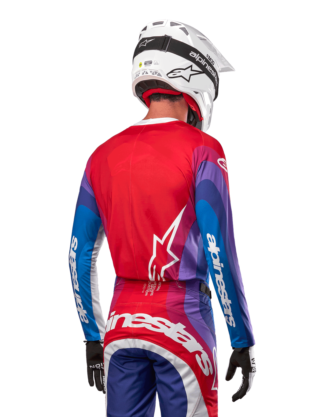 Pilote de motocross de dos portant le maillot Alpinestars 2024 Techstar Pneuma en Blue Mars Red White, avec un dos rouge orné d'un logo étoile blanc et des manches bleues et violettes avec marquage blanc, coordonné à un pantalon assorti et un casque blanc pour la course tout-terrain.