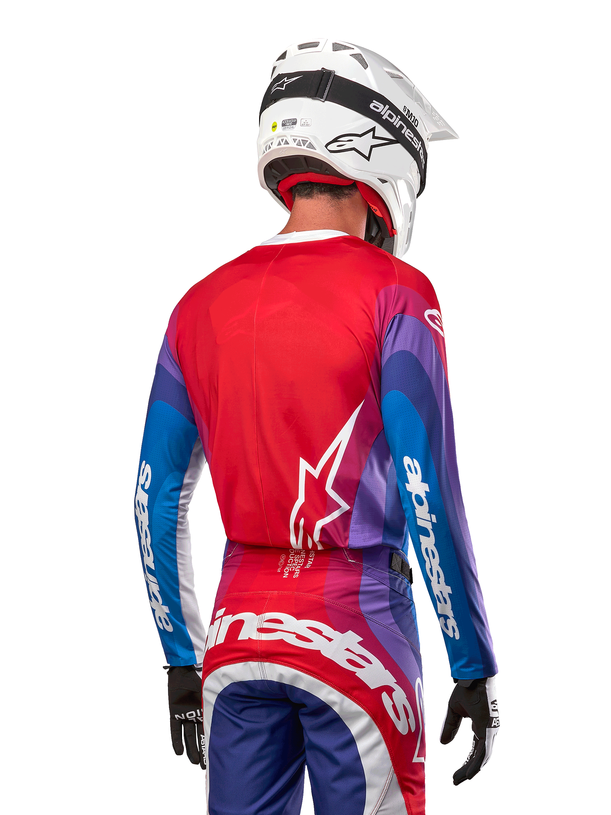 Pilote de motocross de dos portant le maillot Alpinestars 2024 Techstar Pneuma en Blue Mars Red White, avec un dos rouge orné d'un logo étoile blanc et des manches bleues et violettes avec marquage blanc, coordonné à un pantalon assorti et un casque blanc pour la course tout-terrain.