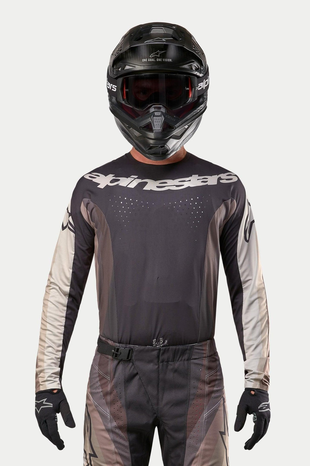 Maillot Alpinestars Techstar Pneuma 2024, maillot de motocross, sable foncé et gris poussière de fer, porté avec un pantalon de motocross assorti et un casque noir, doté d'un logo Alpinestars imposant sur la poitrine et de perforations de ventilation découpées au laser, équipement de course tout-terrain haute performance.