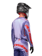 Maillot Alpinestars Techstar Ocuri 2024, maillot de motocross, pourpre et orange vif, vue arrière d'un pilote portant une tenue assortie et un casque noir, avec de grandes lettres Alpinestars orange sur les manches et le bas du dos