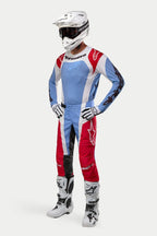 Pilote de motocross portant l'équipement Alpinestars Techstar Ocuri 2024, maillot et pantalon bleu clair, rouge Mars et blanc, casque blanc avec lunettes, gants et bottes blancs et noirs, tenue de course professionnelle pour performance tout-terrain