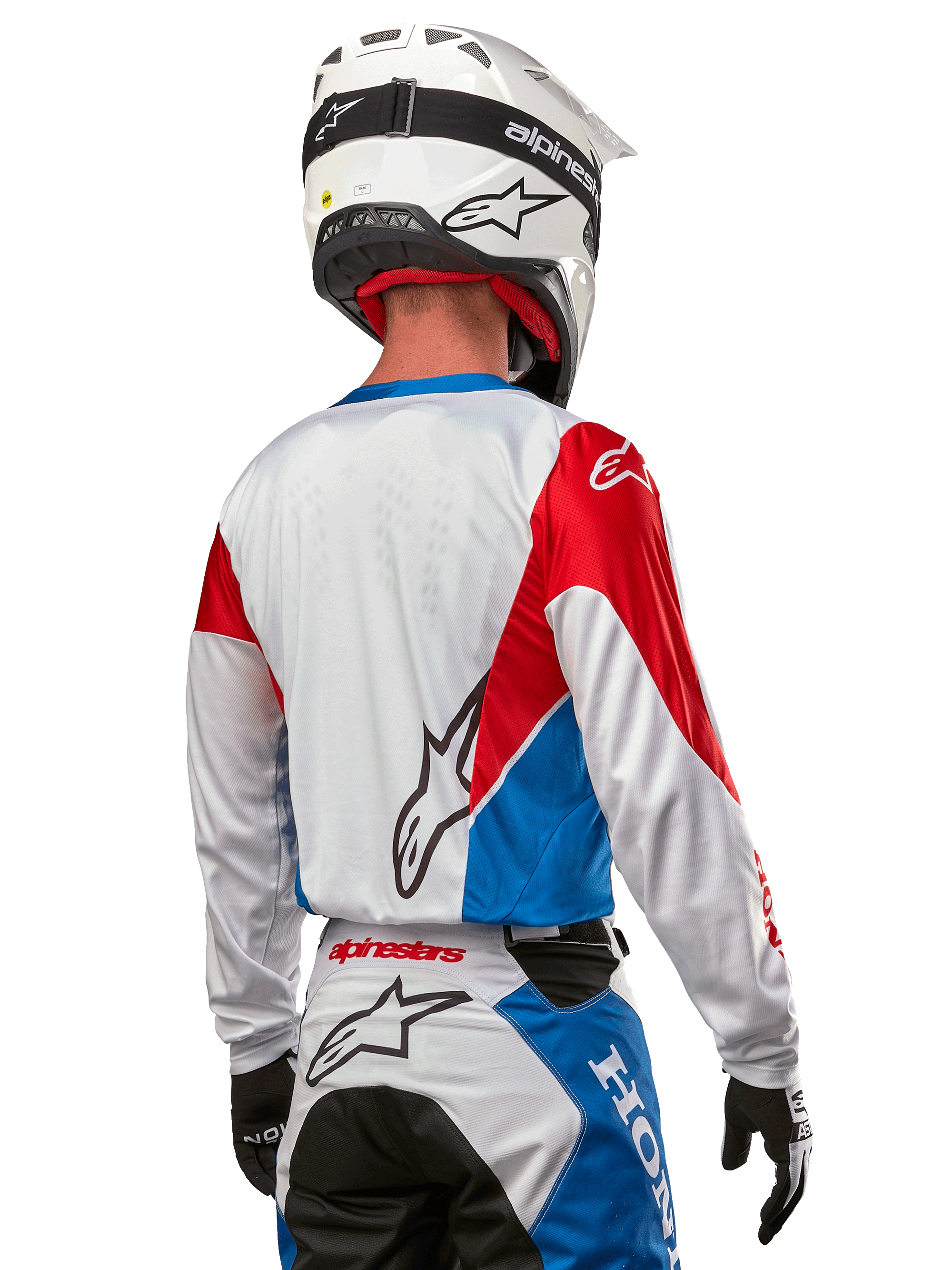 Pilote de motocross portant le maillot Alpinestars Honda Racer Iconic, vue arrière, blanc avec empiècements bleu vif et rouge vif, logo Alpinestars proéminent au dos, associé à un casque de motocross blanc et un pantalon de course assorti.