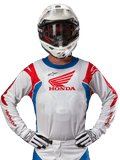 Maillot Honda Racer Iconic, maillot de motocross blanc avec un logo Honda rouge et des accents bleu et rouge vifs, porté par un pilote avec un casque et des gants blancs, équipement de performance pour le tout-terrain et le motocross