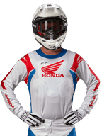 Maillot Honda Racer Iconic, maillot de motocross blanc avec un logo Honda rouge et des accents bleu et rouge vifs, porté par un pilote avec un casque et des gants blancs, équipement de performance pour le tout-terrain et le motocross