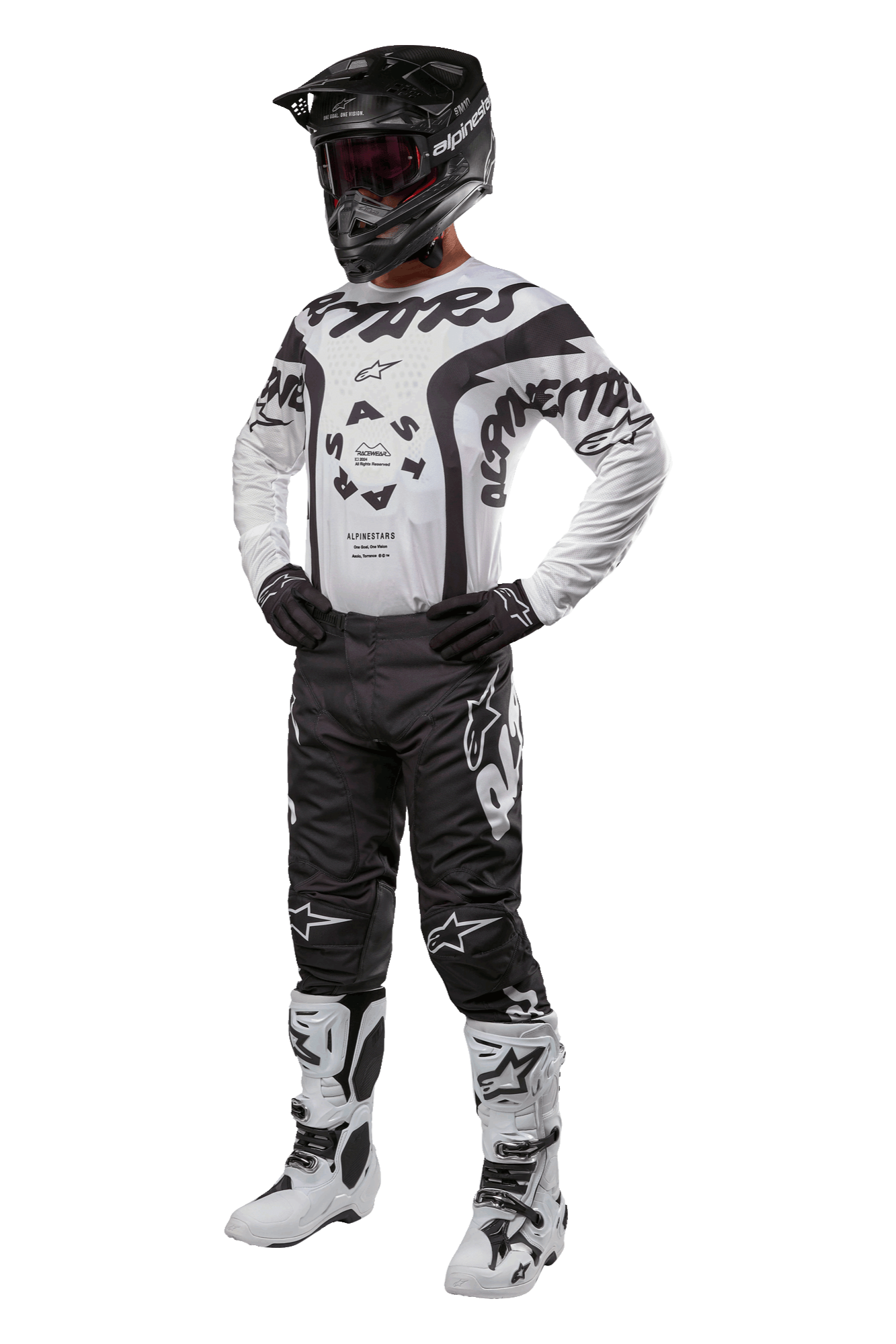 Pilote de motocross portant une tenue complète avec le maillot Alpinestars Racer Hana 2024 en blanc et noir, un pantalon de motocross noir avec des logos blancs, un casque noir, des bottes de course blanches et noires et des gants noirs, tenue de course tout-terrain professionnelle