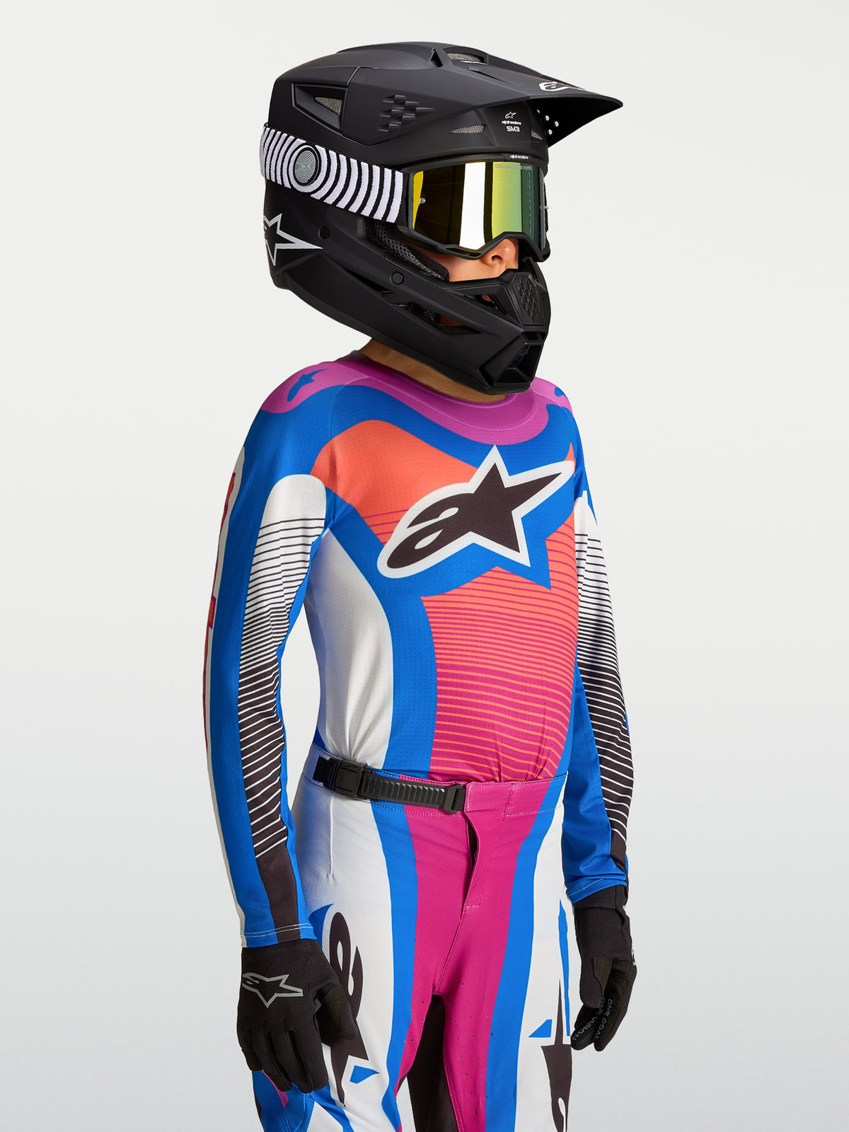 Maillot Alpinestars Supertech Maven Junior, maillot de motocross bleu et corail pour enfant avec un casque de course noir.