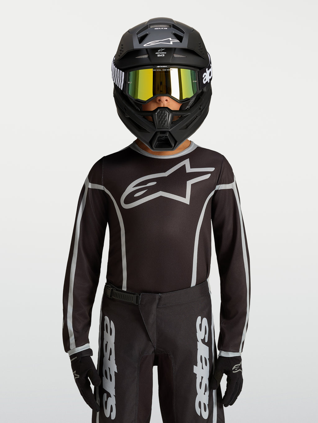 Maillot Alpinestars Fluid Apex V2 Junior, équipement de motocross noir et argenté, porté par un mannequin avec un casque