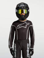 Maillot Alpinestars Fluid Apex V2 Junior, équipement de motocross noir et argenté, porté par un mannequin avec un casque