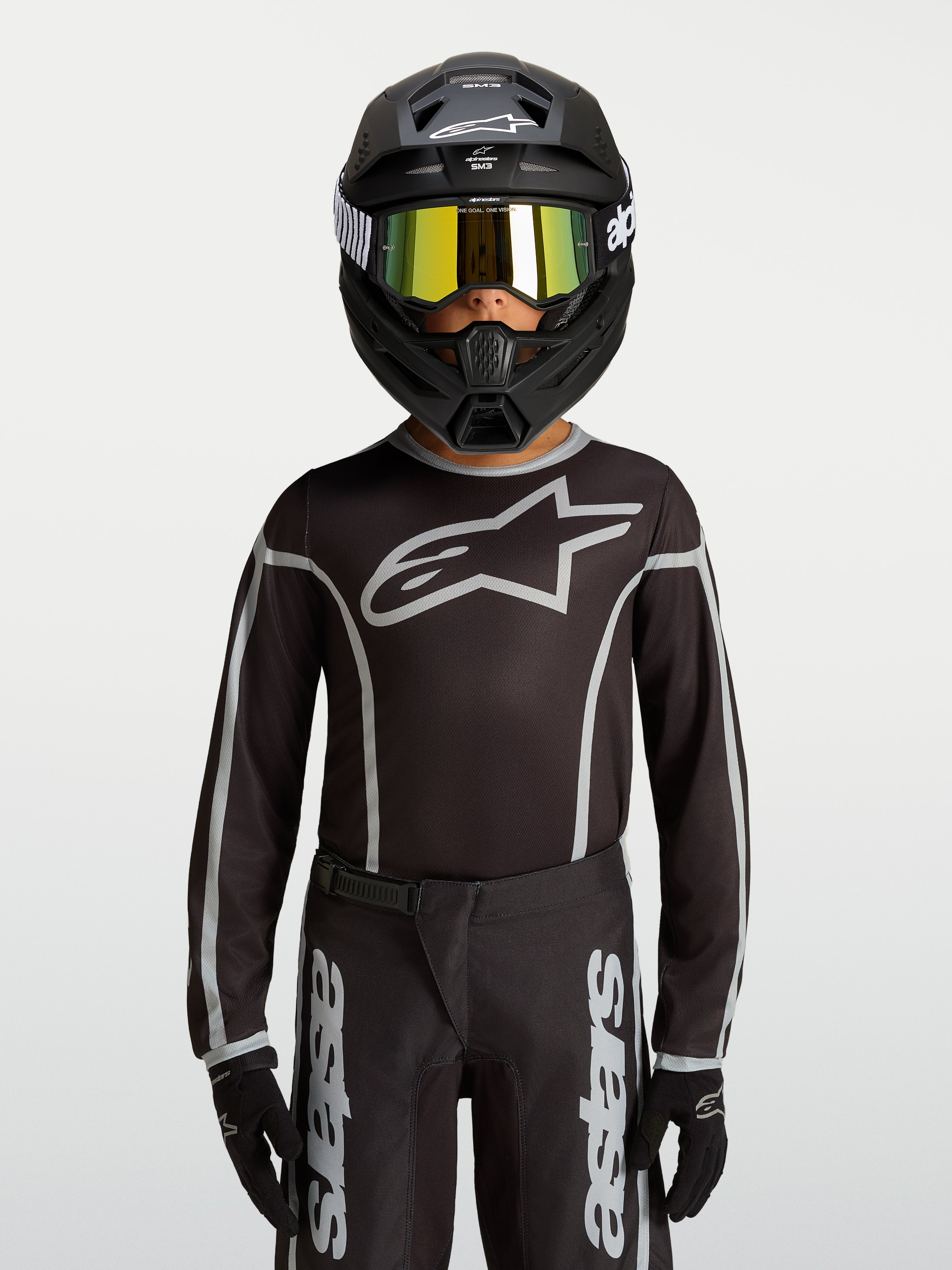 Maillot Alpinestars Fluid Apex V2 Junior, équipement de motocross noir et argenté, porté par un mannequin avec un casque