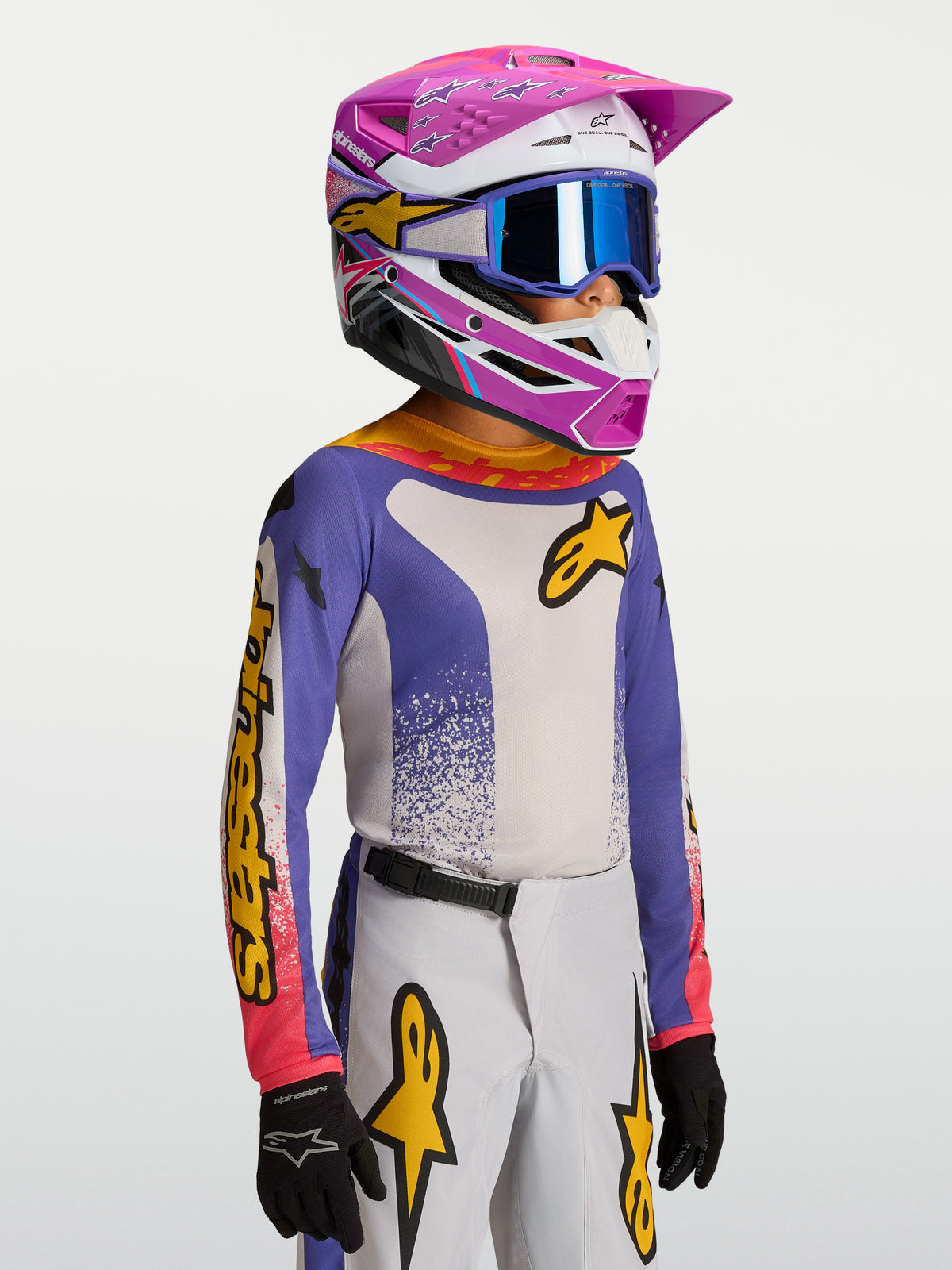 Maillot Fluid Drag Junior 2027 Alpinestars, maillot de motocross pour enfant, bleu et blanc avec accents jaunes, porté par un jeune pilote avec casque et masque de protection.
