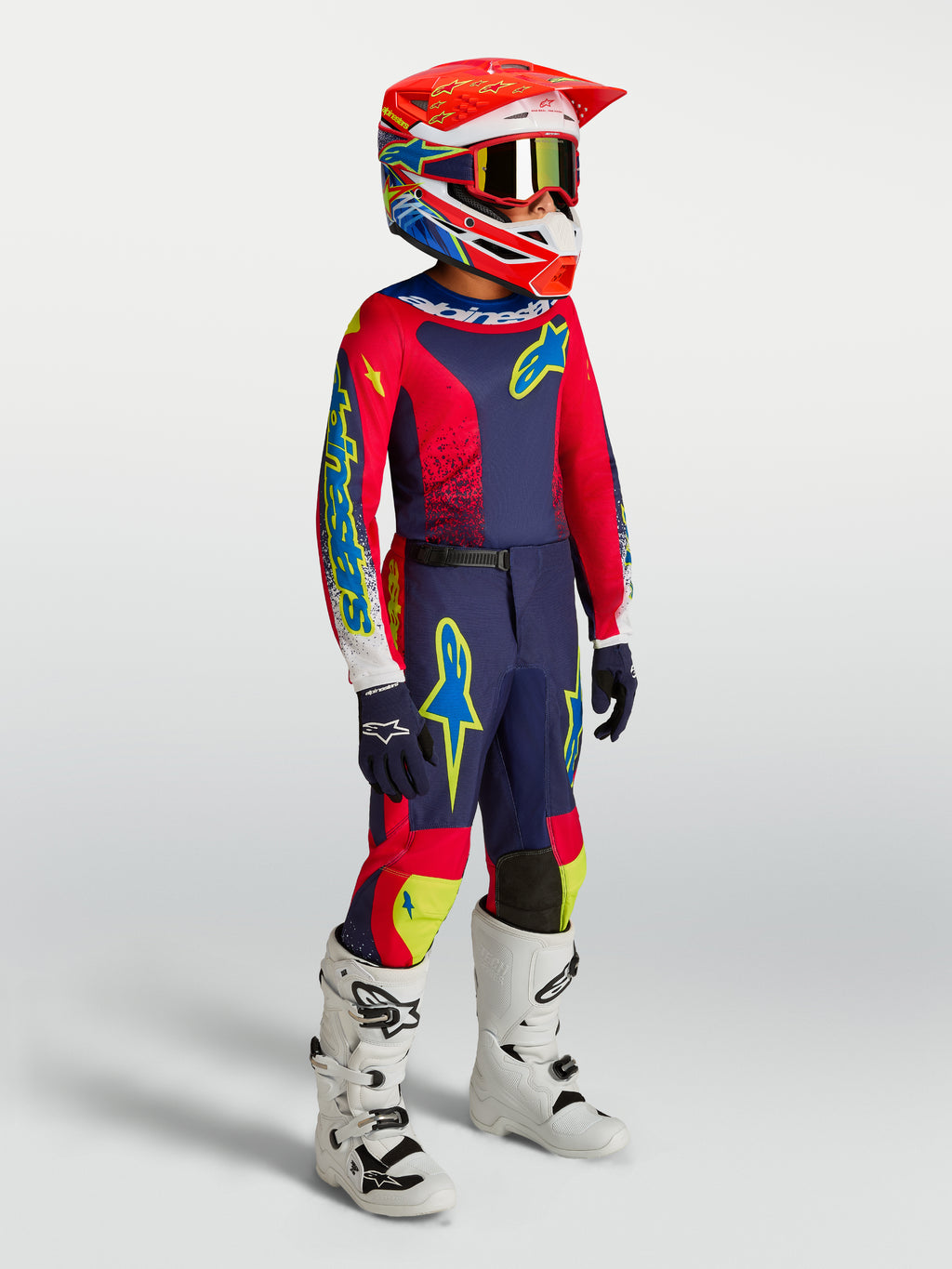 Ensemble Fluid Drag Junior 2027 Alpinestars, kit de motocross bleu marine et rouge feu, bottes blanches, porté par un pilote.
