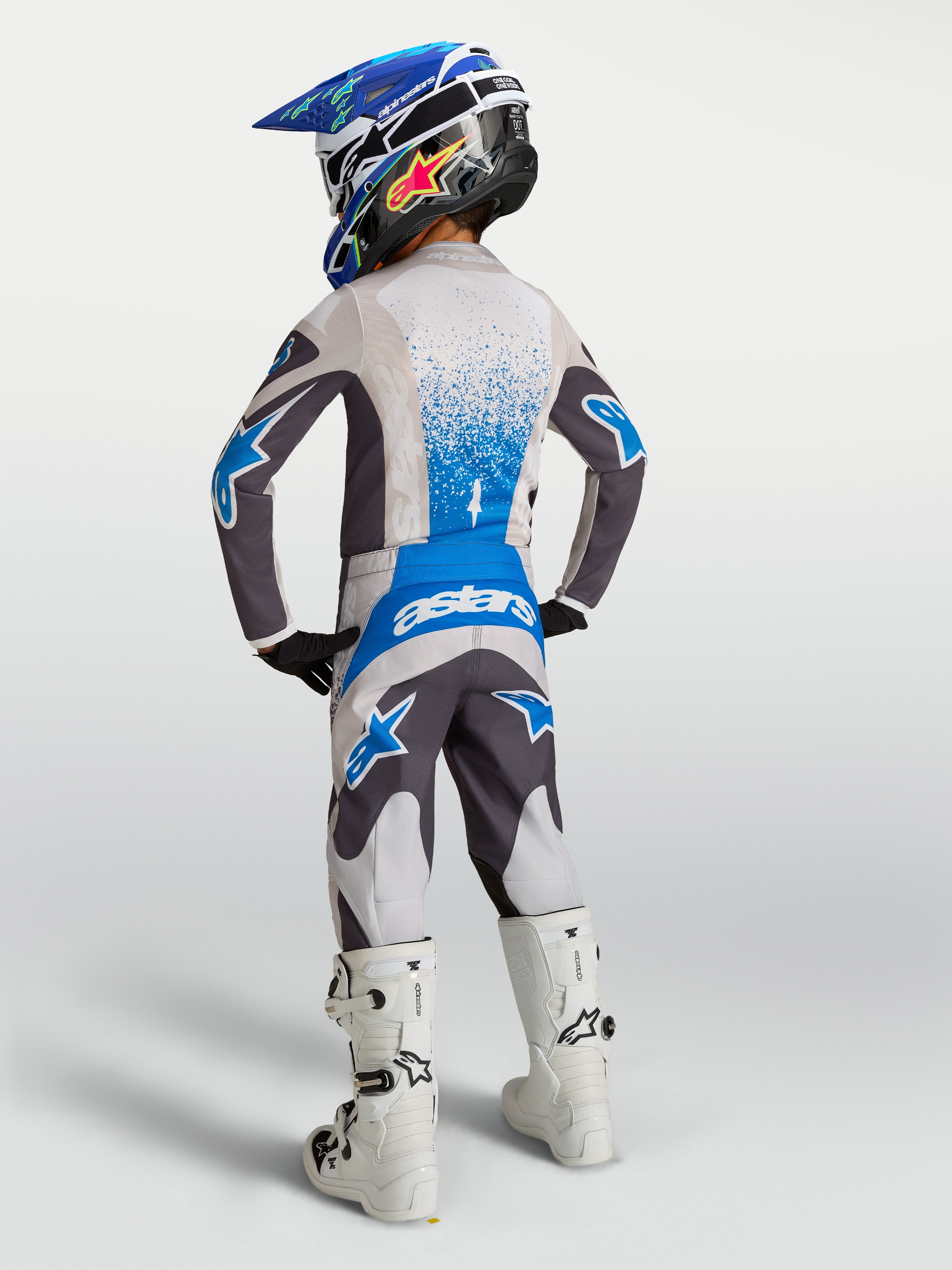 Ensemble de motocross Alpinestars Fluid Drag junior, maillot et pantalon gris et bleus, vue de dos sur un jeune pilote.