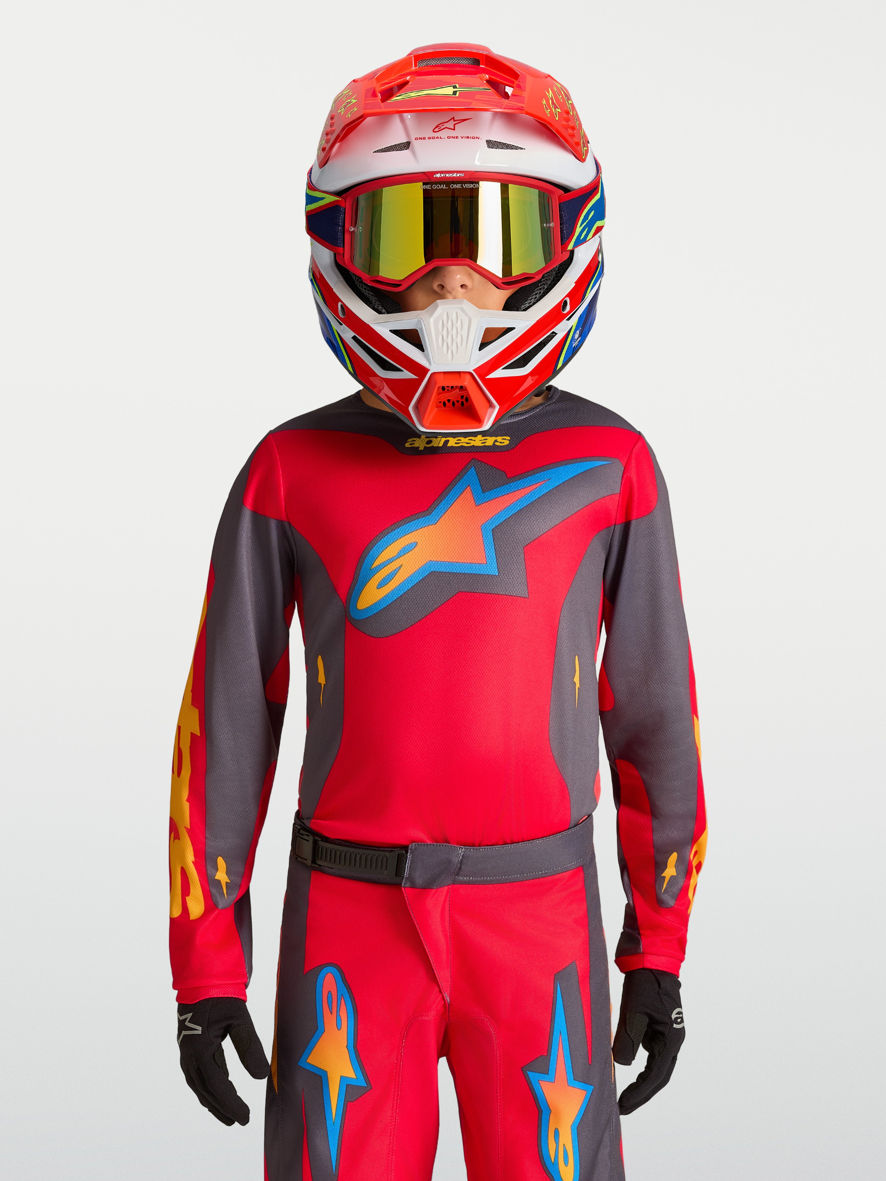 Maillot Alpinestars Fluid Hunt junior 2027, équipement de motocross rouge et gris, porté avec un casque de course.