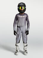 Alpinestars maillot et ensemble Fluid Amber junior 2027, tenue de motocross grise et sable, casque noir et bottes blanches.