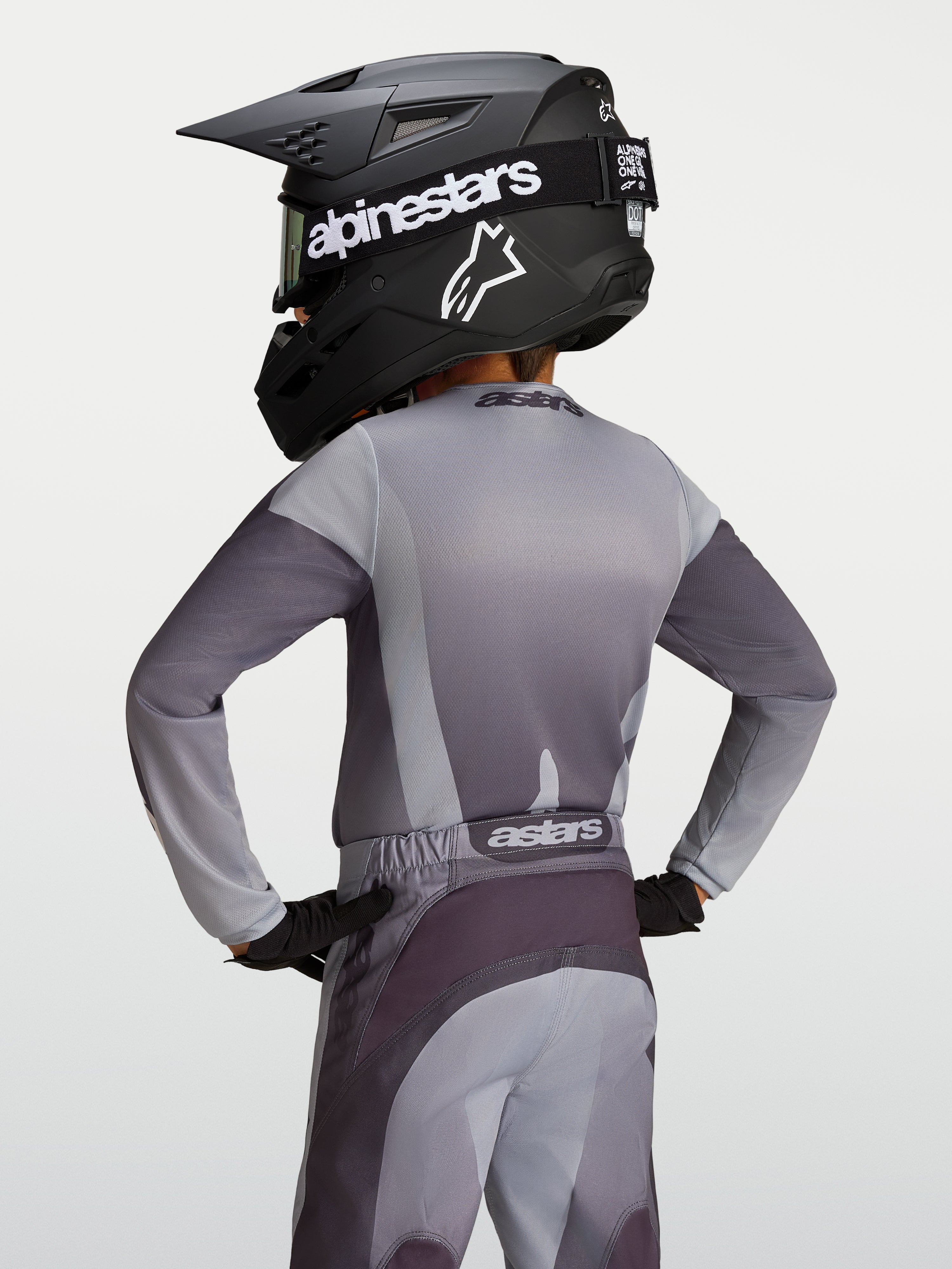 Alpinestars Maillot Fluid Amber Junior, maillot de motocross pour enfant, gris et sable, tissu respirant évacuant l'humidité, vue de dos sur un jeune pilote avec casque.