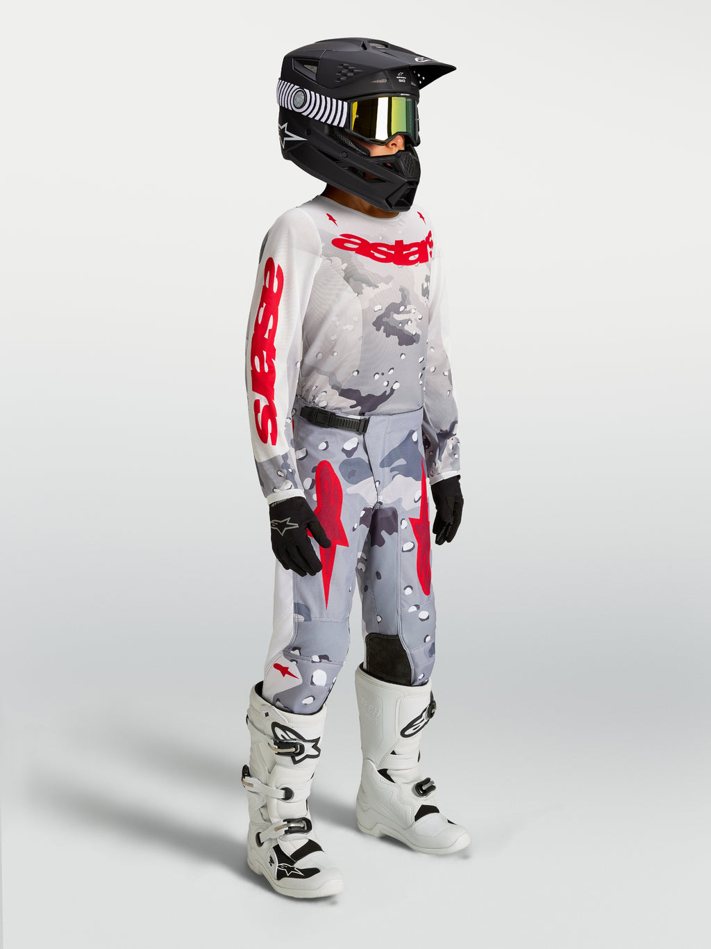 Ensemble Fluid Lone Junior Alpinestars, maillot et pantalon de motocross gris camouflage et rouge avec bottes blanches.