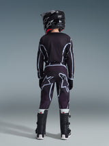 Alpinestars Maillot Junior Fluid Apex 2026, jeune pilote de motocross vu de dos, maillot noir et gris, pantalon assorti avec larges logos blancs, casque noir et bottes Tech Series noir et blanc, tenue de performance complète pour le tout-terrain.