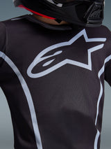 Maillot Alpinestars 2026 Youth Fluid Apex, gros plan sur le design de la poitrine, noir et gris, arborant un logo en étoile gris clair proéminent et des liserés athlétiques, porté avec un casque noir, équipement de motocross performant pour jeunes pilotes