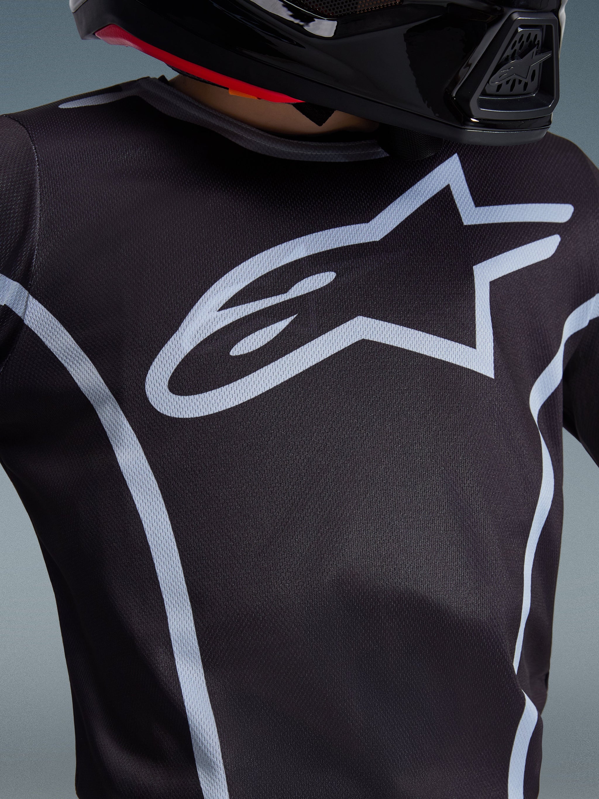 Maillot Alpinestars 2026 Youth Fluid Apex, gros plan sur le design de la poitrine, noir et gris, arborant un logo en étoile gris clair proéminent et des liserés athlétiques, porté avec un casque noir, équipement de motocross performant pour jeunes pilotes