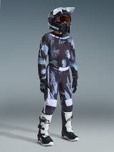 Youth motocross rider wearing the 2026 Youth Fluid Lahnd Jersey in Iron Camo, black and grey camouflage pattern, matching pants, black Alpinestars helmet with goggles, black and white boots, and black gloves, complete youth motocross racing gear