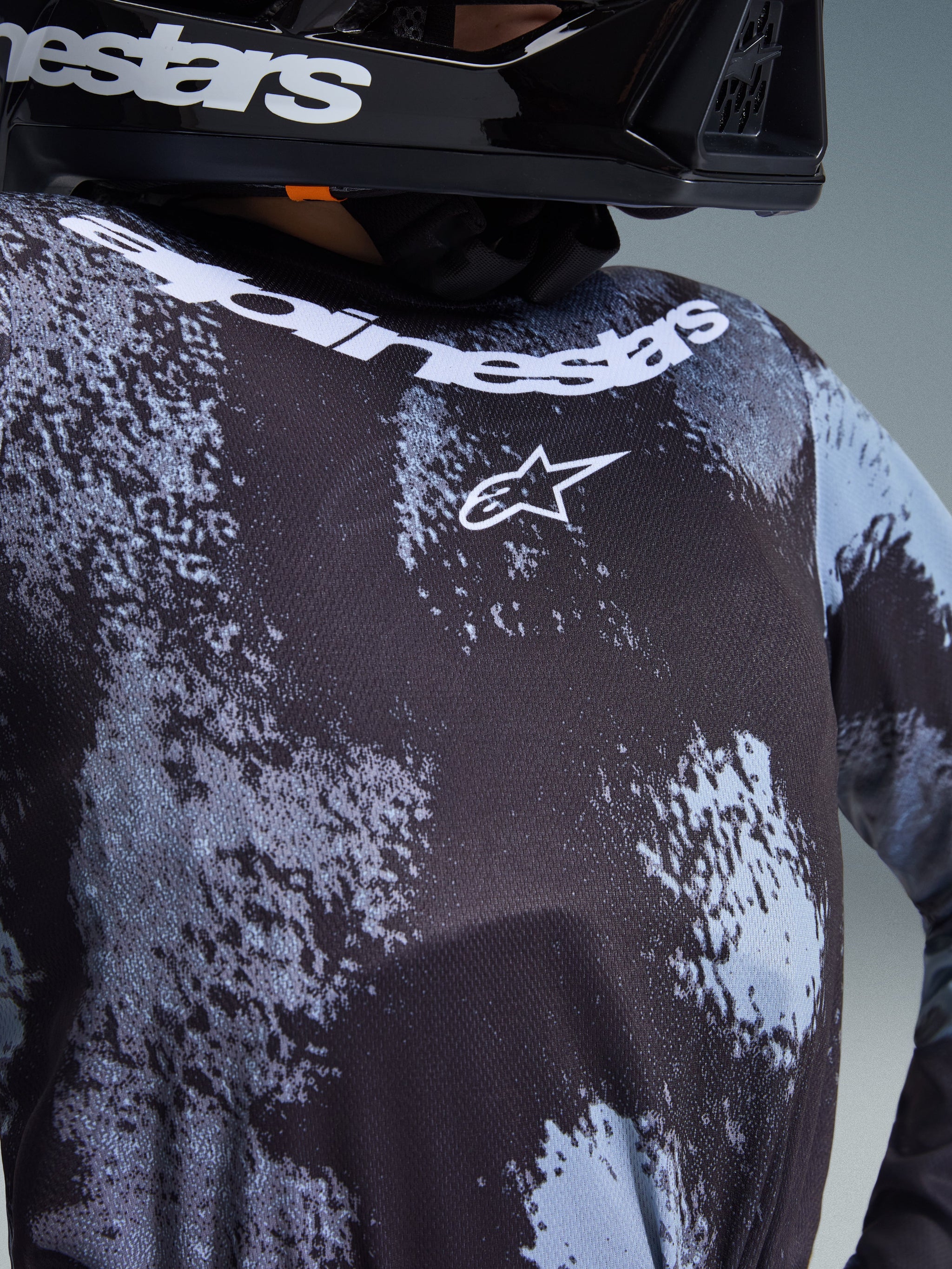 Close-up of the Alpinestars 2026 Youth Fluid Lahnd Jersey in Iron Camo, featuring a black and grey camouflage pattern, white Alpinestars logo on the chest, and brand name along the neckline, worn by a rider in a black helmet.
