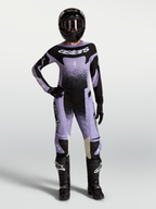 Pantalon Stella Techstar Swan Alpinestars, pantalon de motocross pour femme, violet et noir, conçu pour la performance tout-terrain, porté par une pilote avec tenue complète et casque.