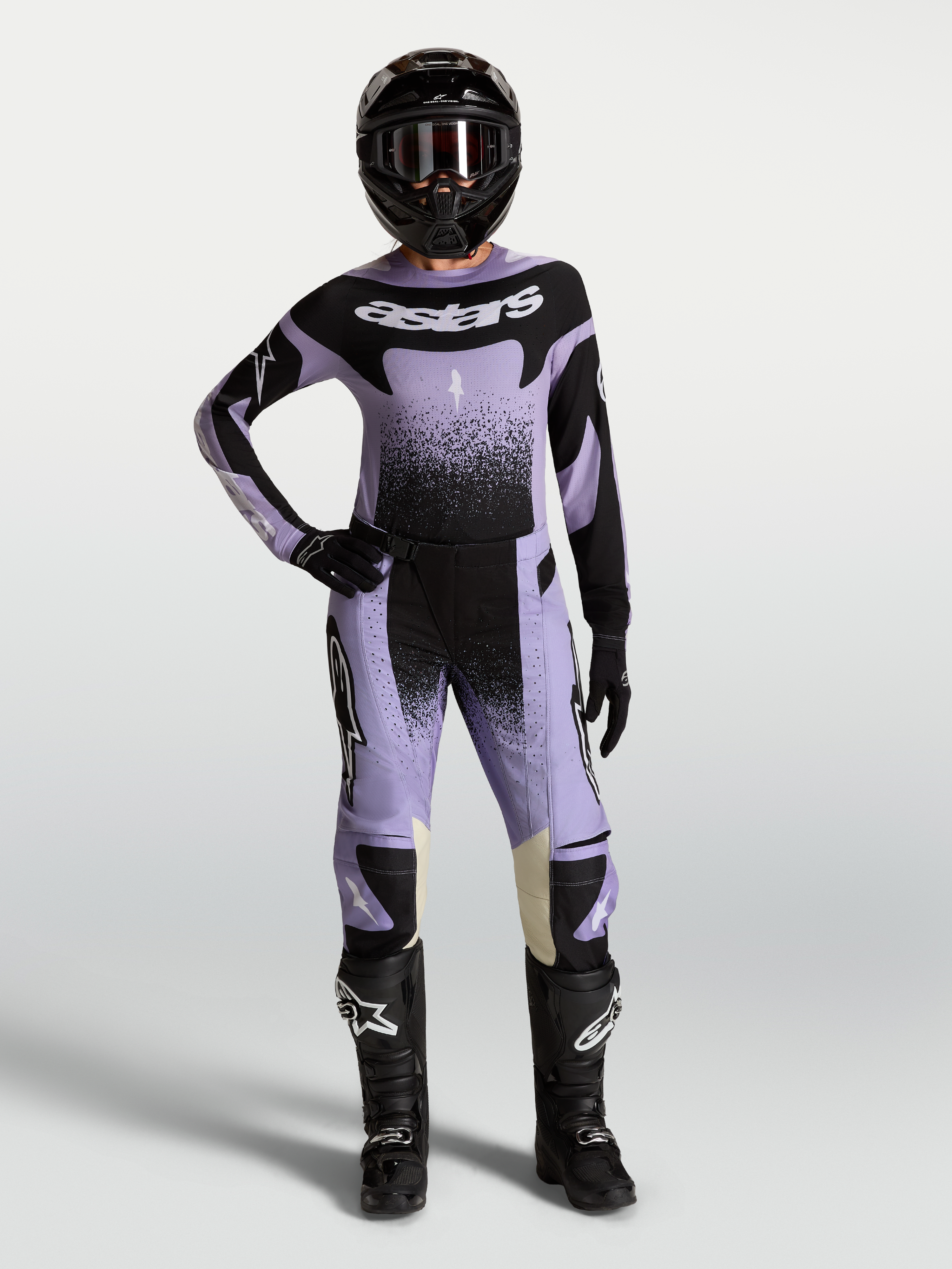 Pantalon Stella Techstar Swan Alpinestars, pantalon de motocross pour femme, violet et noir, conçu pour la performance tout-terrain, porté par une pilote avec tenue complète et casque.