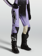Alpinestars Stella Techstar Swan, pantalon de motocross pour femme, coloris violet et noir, porté avec des bottes et gants noirs, construction en poly-tissu durable et cuir aux genoux pour une performance tout-terrain optimale