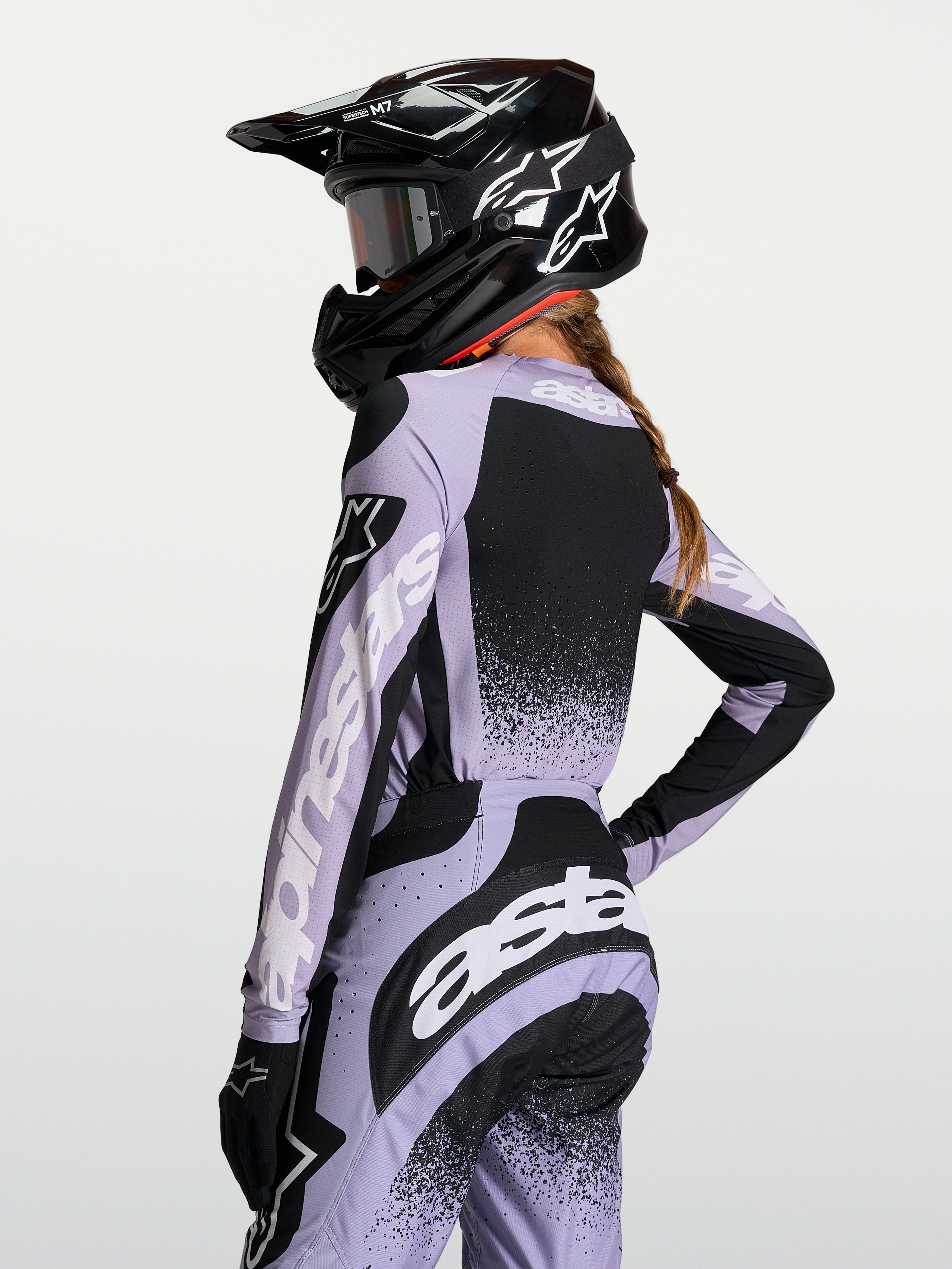 Maillot Stella Techstar Swan Alpinestars, haut de motocross pour femme, violet et noir, tissu respirant et coupe de course, vue de dos avec casque et logos blancs