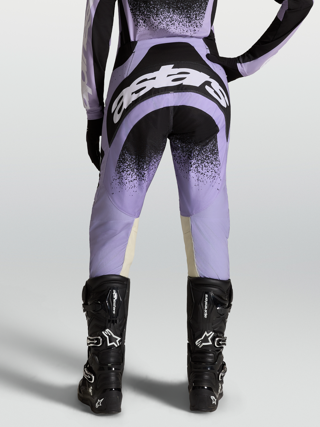 Alpinestars Stella Techstar Swan, pantalon de motocross pour femme, violet et noir, vue de dos avec logos blancs, porté par un mannequin avec des bottes de moto noires