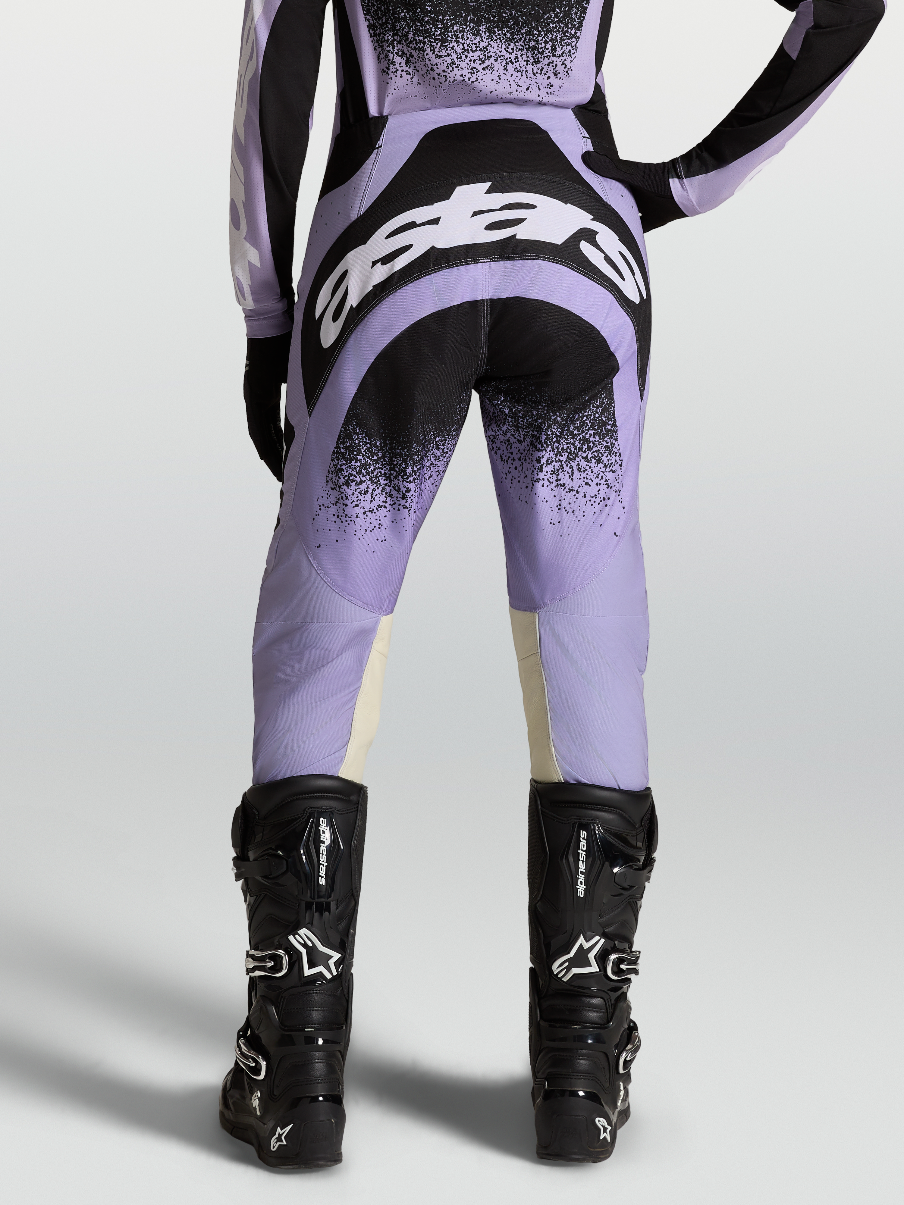 Alpinestars Stella Techstar Swan, pantalon de motocross pour femme, violet et noir, vue de dos avec logos blancs, porté par un mannequin avec des bottes de moto noires
