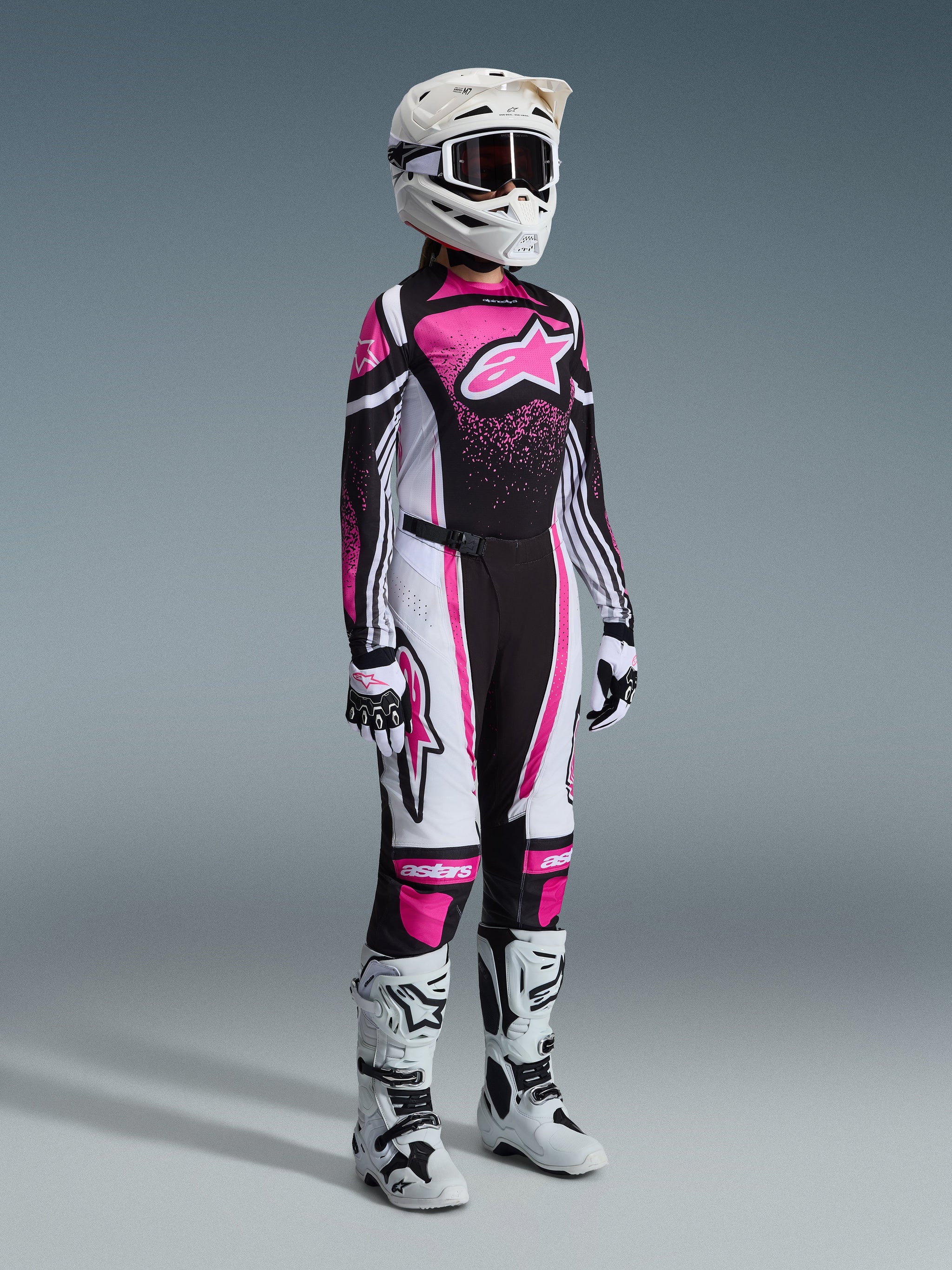 Motocross rider wearing the Alpinestars 2026 Woman Stella Techstar Nomur Jersey in Black White and Fuchsia, styled with matching motocross pants, a white helmet with goggles, and white boots, full professional racing gear set for women.