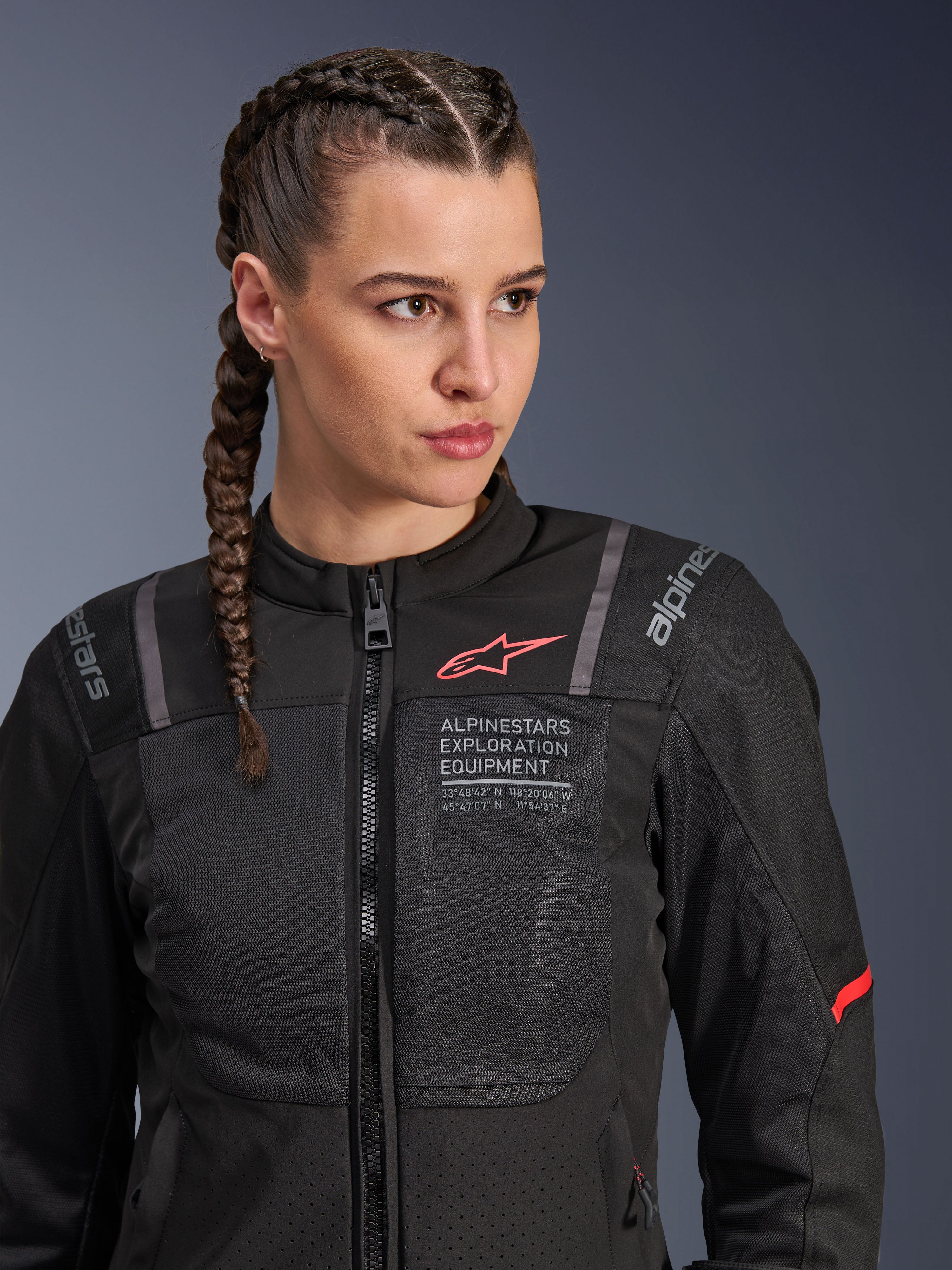 Veste Alpinestars Stella ST-2 Air, veste de moto pour femme en noir, avec panneaux en mesh pour la circulation de l'air, marquage « Alpinestars Exploration Equipment » avec coordonnées, logo rouge sur la poitrine, portée par un mannequin aux cheveux tressés