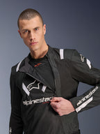 Veste Alpinestars T-Stunt Air, veste de moto noire et blanche, modèle masculin montrant le panneau avant modulaire partiellement dézippé révélant des couches de mesh pour la circulation de l'air, logos Alpinestars blancs sur la poitrine et les manches, design sportif pour la route