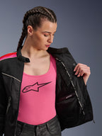 Motarde portant la veste Alpinestars Stella T-Dyno Air en Noir Rouge Vif Fuchsia, présentée partiellement ouverte pour révéler le compartiment imperméable interne, portée sur un débardeur rose à logo, mettant en avant les panneaux en maille respirante et la coupe biker ajustée.