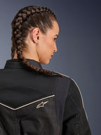 Femme portant la veste Alpinestars Stella T-Dyno Air, vue arrière en gros plan sur les épaules et l'empiècement, noir avec panneaux en maille 3D respirante, liseré blanc et petit logo Astars, mannequin aux cheveux tressés, équipement de moto urbain