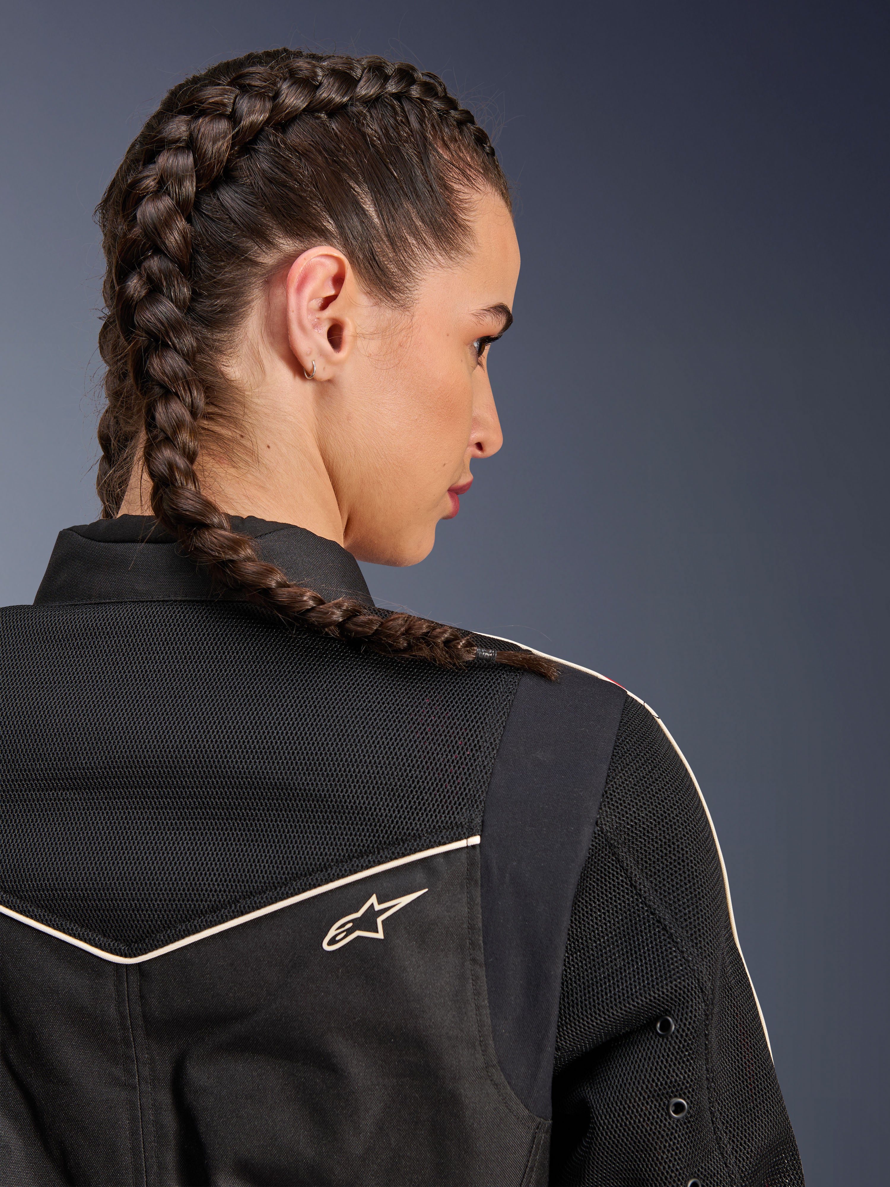 Femme portant la veste Alpinestars Stella T-Dyno Air, vue arrière en gros plan sur les épaules et l'empiècement, noir avec panneaux en maille 3D respirante, liseré blanc et petit logo Astars, mannequin aux cheveux tressés, équipement de moto urbain