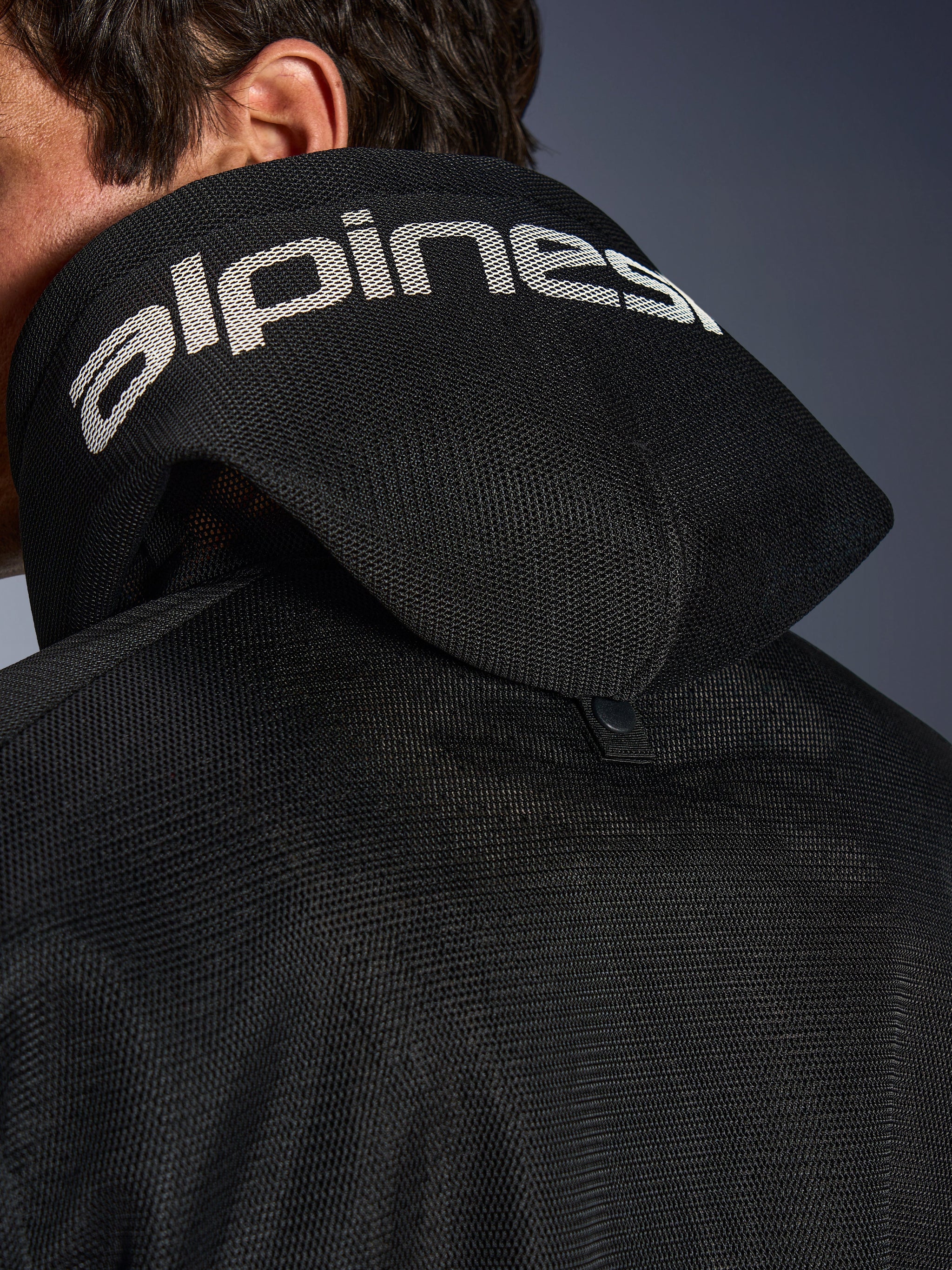 Alpinestars Chrome Superairflow Hoodie, Black, Detail view of the 3D mesh hood with white alpinestars branding across the top, showing the rear stabilization snap button, ventilated textile motorcycle gear for extreme heat