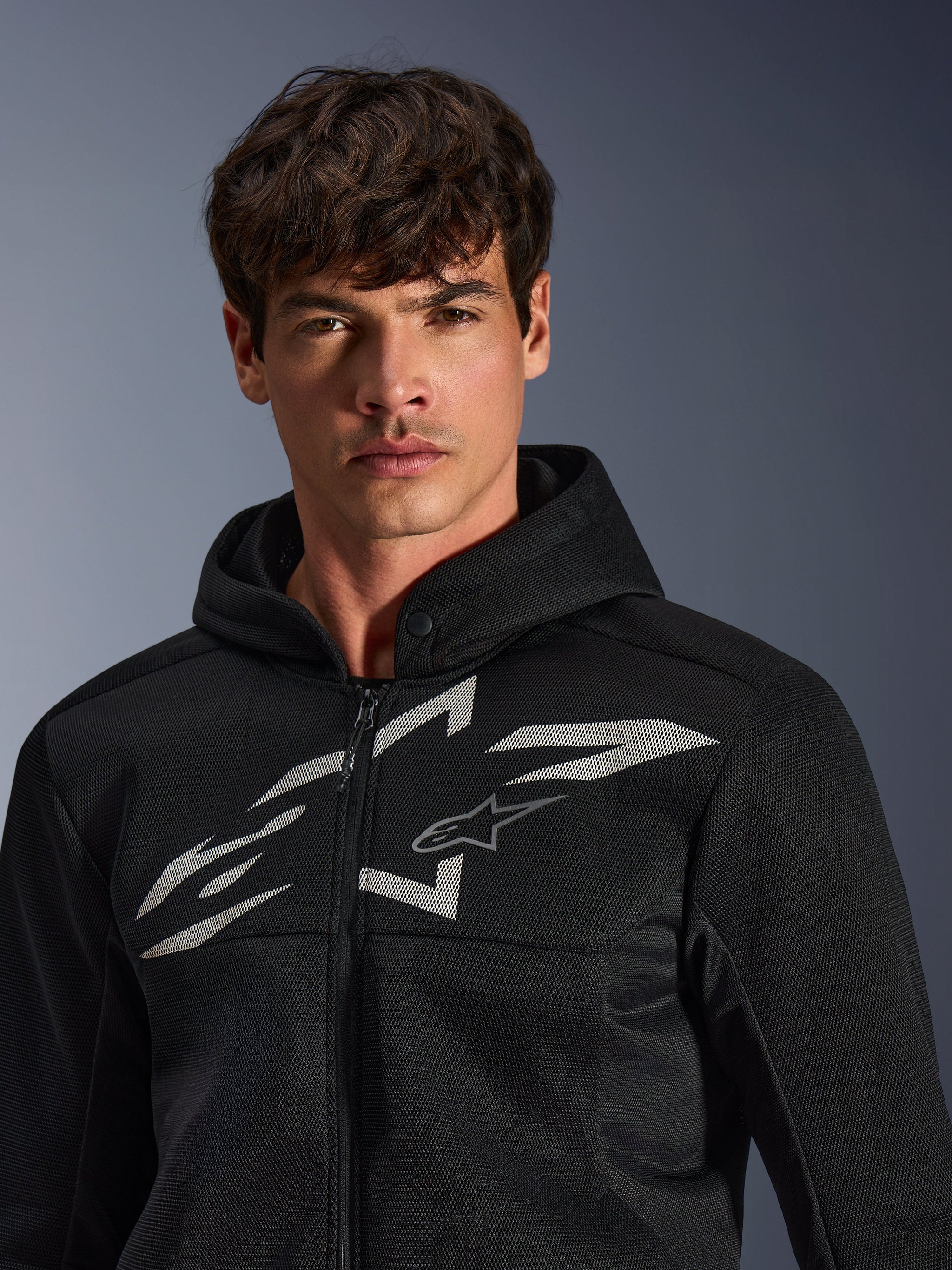 Alpinestars Chrome Superairflow Hoodie, Black motorcycle hoodie, features 3D mesh construction with a large white graphic logo on the chest, worn by a model, urban sport riding apparel with a modern ventilated design